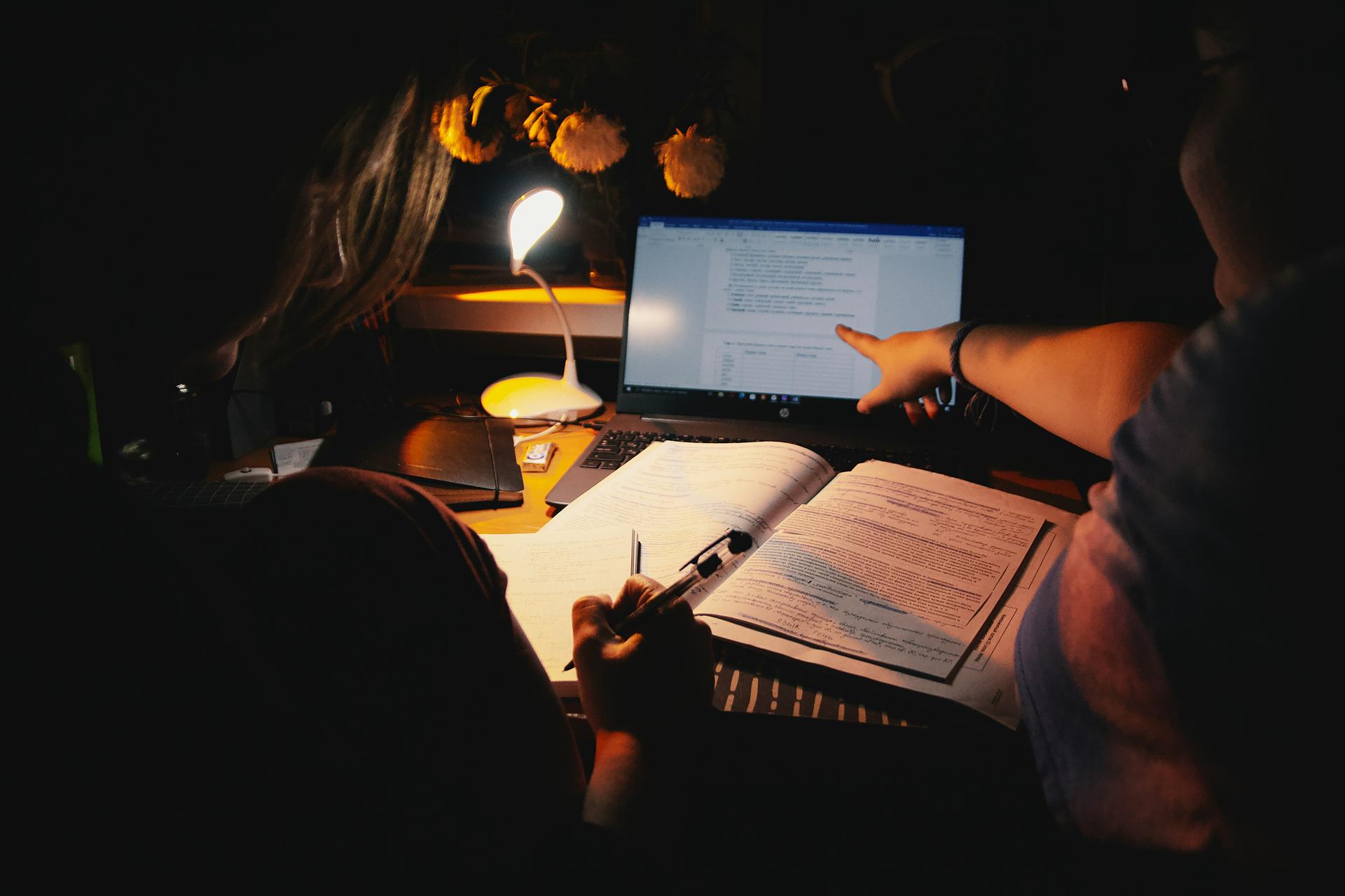 Two students studying together at a desk with books and a laptop
